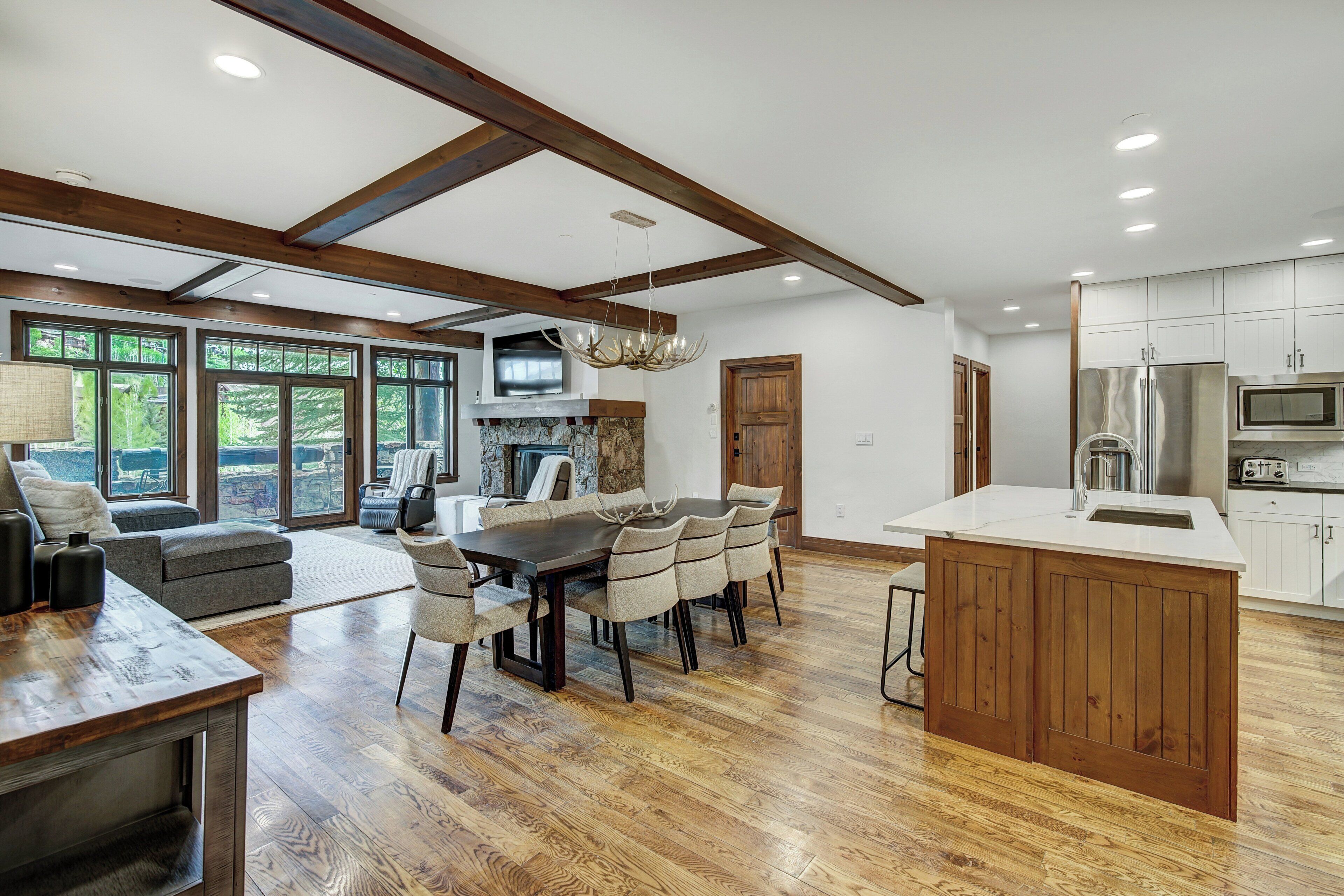Una cocina amplia con vigas de madera, un comedor con una mesa grande y sillas, y vistas al exterior a través de ventanas grandes.