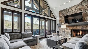A modern living room with a stone fireplace, large windows, and a cozy seating area. - Bachelor Gulch Village by Vail Resorts (Avon)