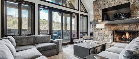 A modern living room with a stone fireplace, large windows, and a cozy seating area.