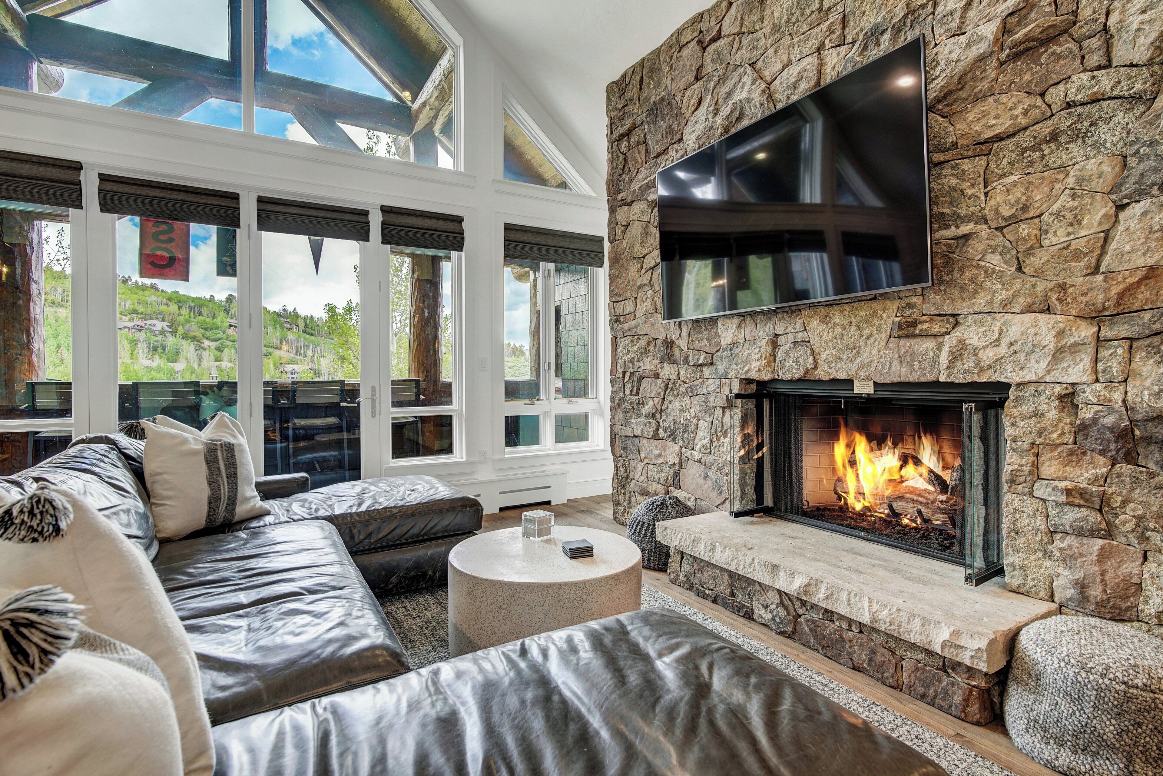 Una sala de estar moderna con chimenea de piedra, sofás de cuero y grandes ventanales con vistas al exterior.