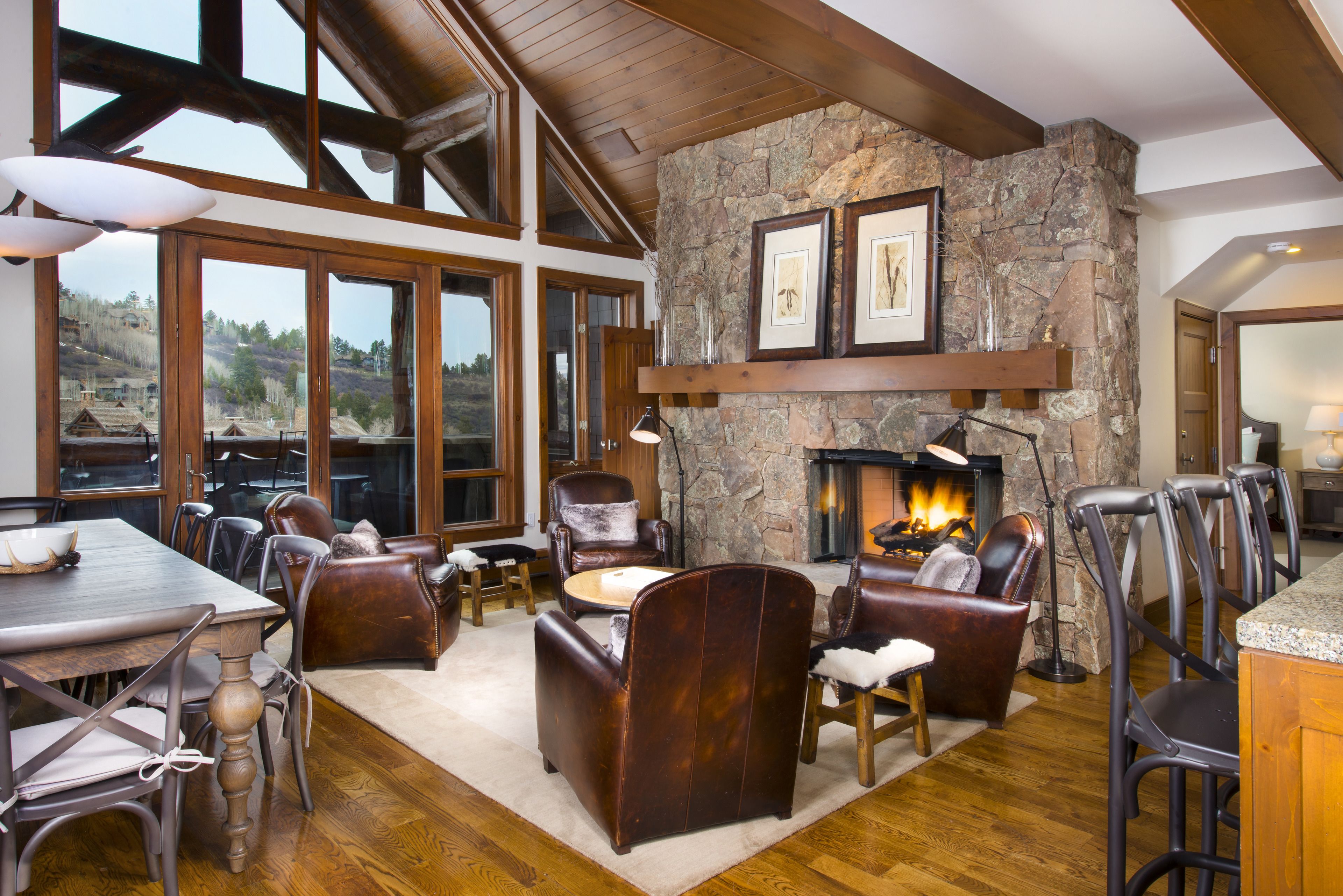 Un salón amplio con chimenea de piedra, vigas de madera y ventanas grandes que ofrecen vistas al exterior.