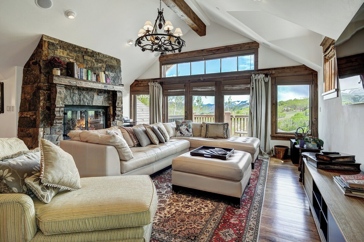 A spacious living room with a stone fireplace, large windows, and a cozy seating area.