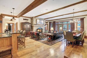 A spacious living room with a fireplace, wooden beams, a dining area with chairs, and a kitchen with a bar. - Bachelor Gulch Village by Vail Resorts (Avon)