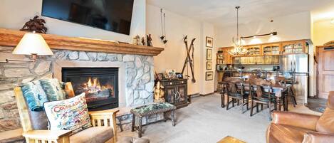 A cozy living room with a stone fireplace, a flat-screen TV, and a dining area with wooden furniture.