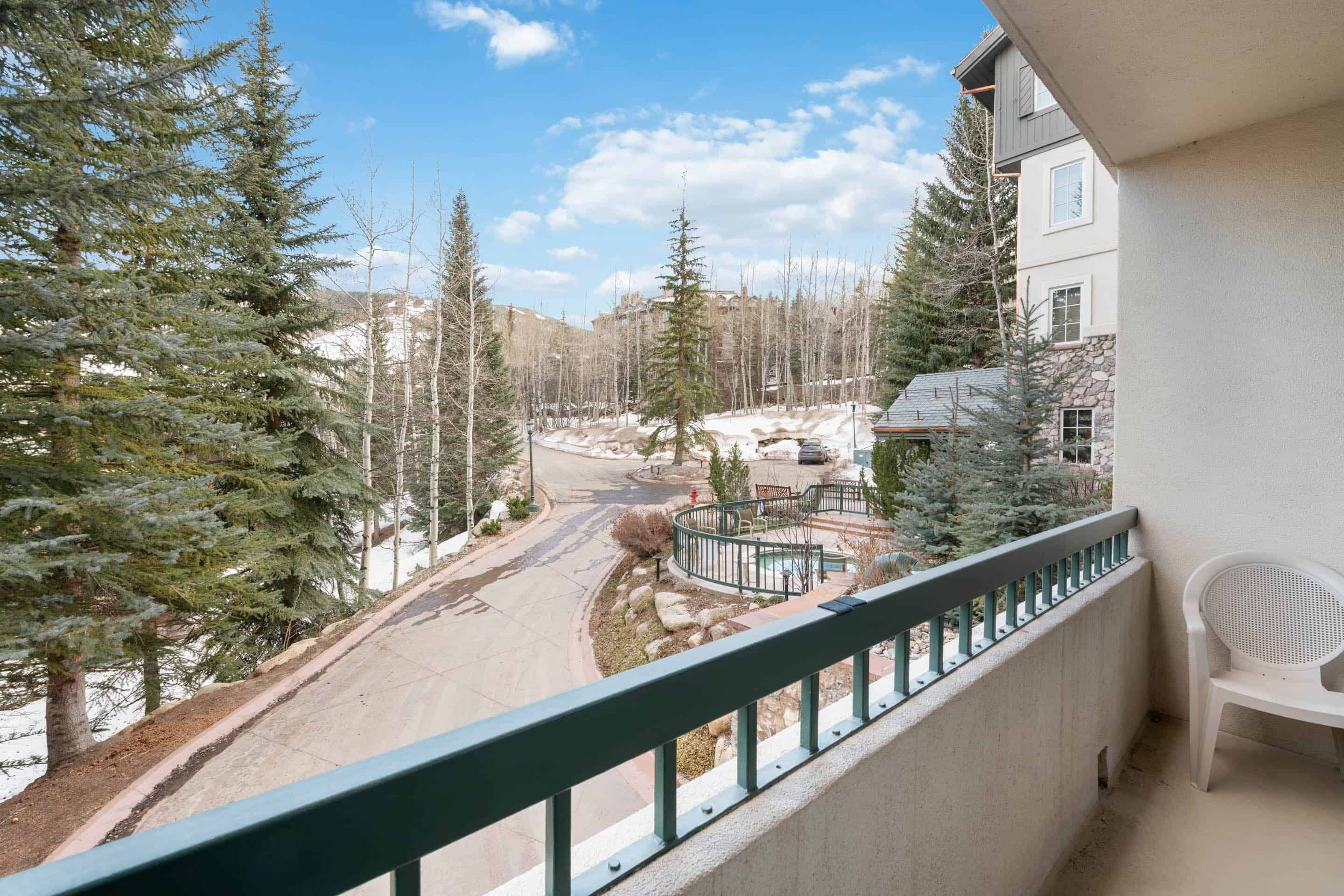 A balcony with a view of a snow-covered landscape, a paved road, and a building with a stone facade.