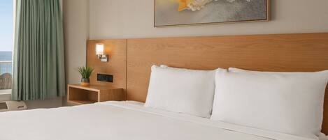 A hotel room with a large bed, a wooden headboard, a nightstand with a lamp, a potted plant, and a painting on the wall.