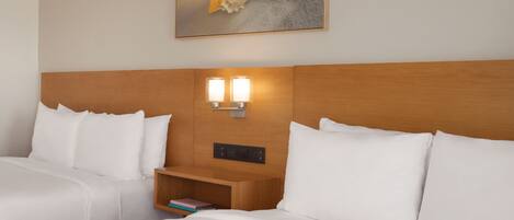 Ein Hotelzimmer mit einem Holz-Kopfteil, zwei weißen Betten, einem Nachttisch mit Lampe und einem Bild an der Wand.