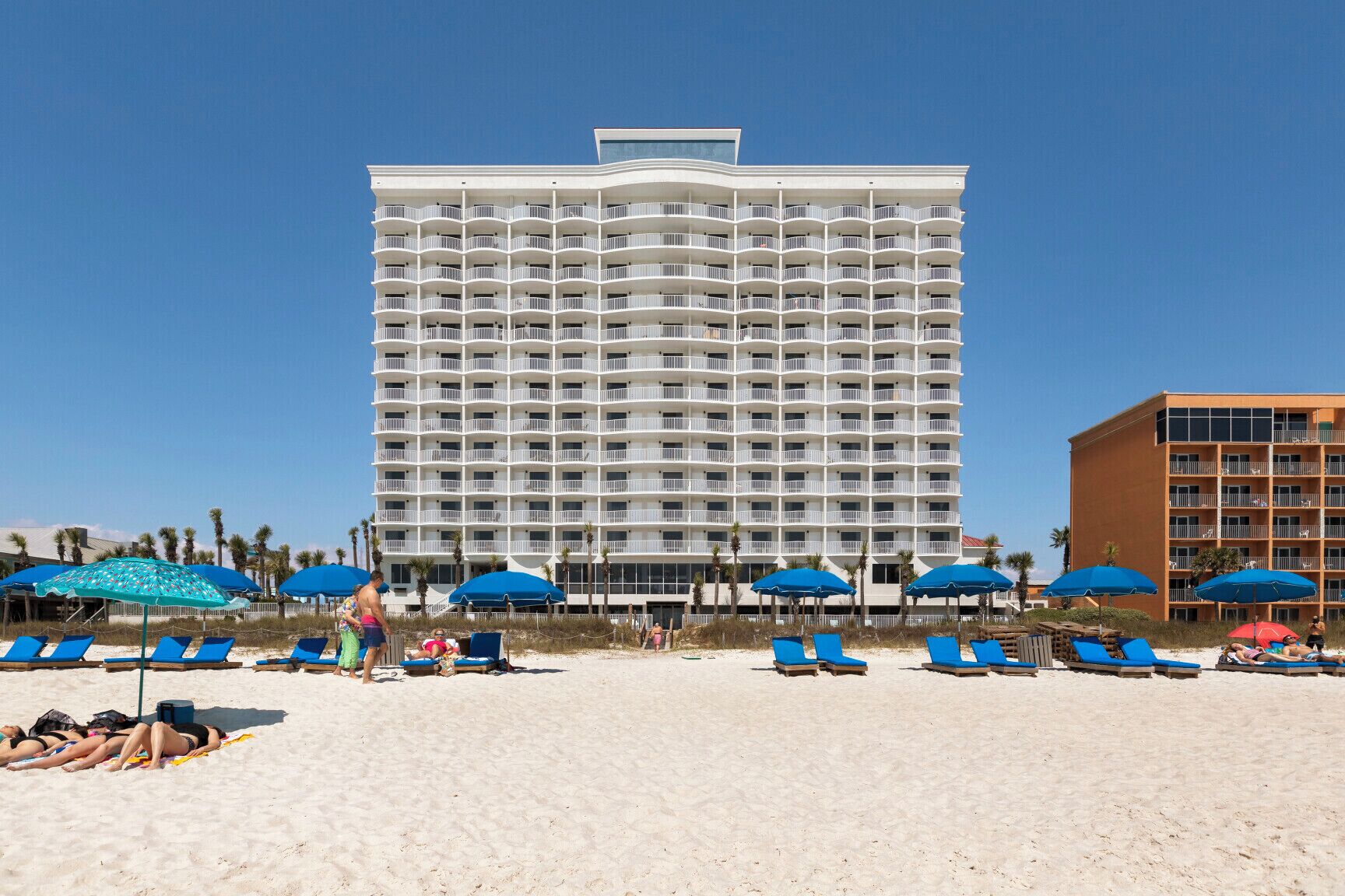 Ein Strandhotel mit mehreren Balkonen, Liegestühlen und Sonnenschirmen.