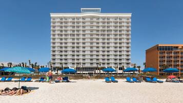 Ein Strandhotel mit mehreren Balkonen, Liegestühlen und Sonnenschirmen.