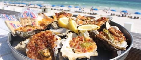 A tray of oysters on the half shell with lemon wedges and crackers on a beach setting.