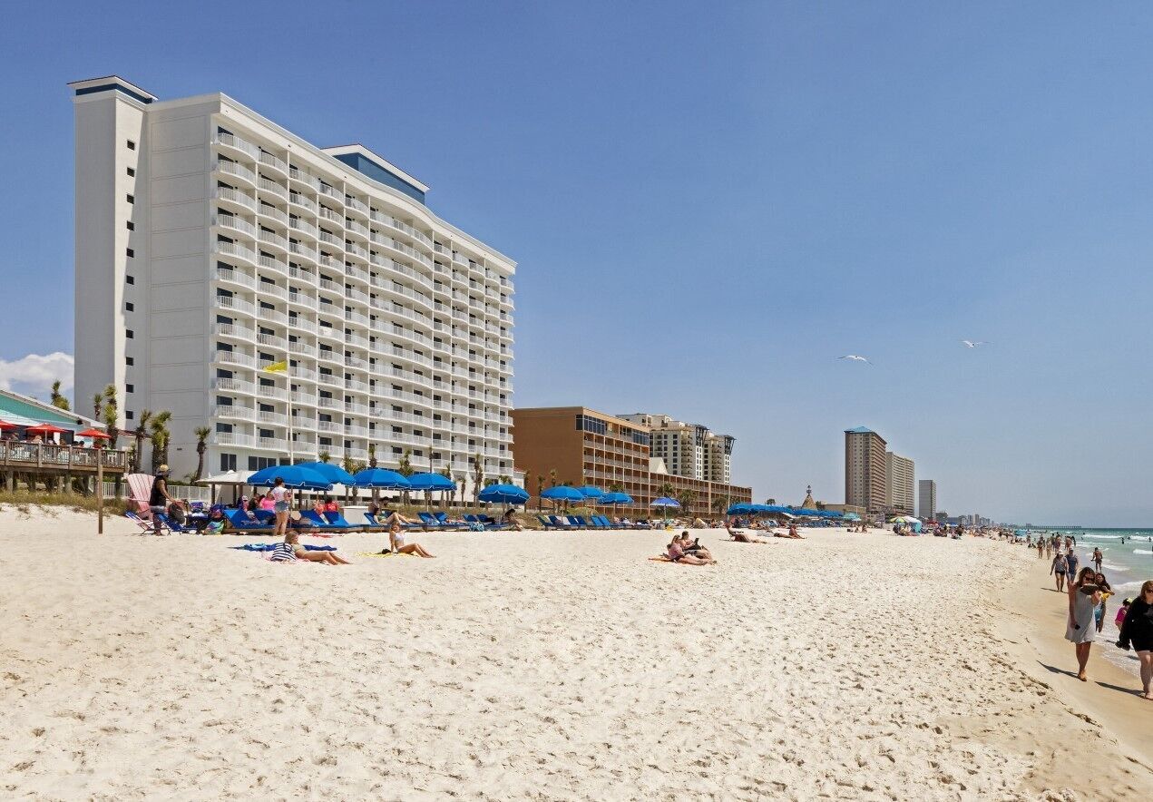 Une plage avec un grand hôtel, des transats et des parasols.