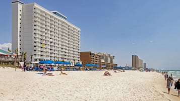 Una playa con un hotel grande, sillas de playa y sombrillas.