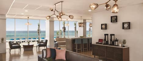 A modern hotel lobby with a large seating area, a bar, and a view of the ocean.