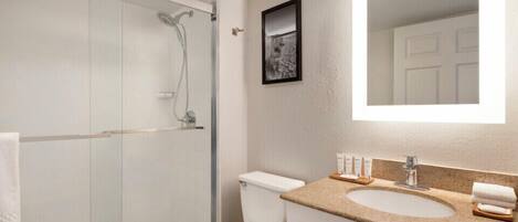 Une salle de bain moderne avec une douche à parois de verre, des toilettes blanches, un lavabo avec un plan de travail en granit et un tableau encadré au mur.