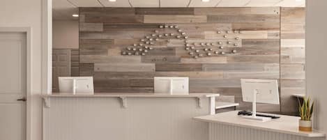 Un comptoir d’accueil avec un mur en bois décoratif, un plan de travail blanc et une plante en pot.
