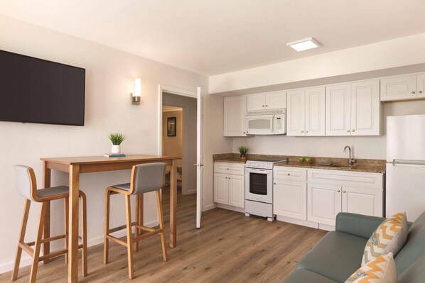 A compact kitchen with white cabinets, a microwave, a stove, and a refrigerator. There is a wooden dining table with two chairs and a green sofa with patterned cushions. - Radisson Beachfront Hotel - Panama City Beach (Panama City Beach)