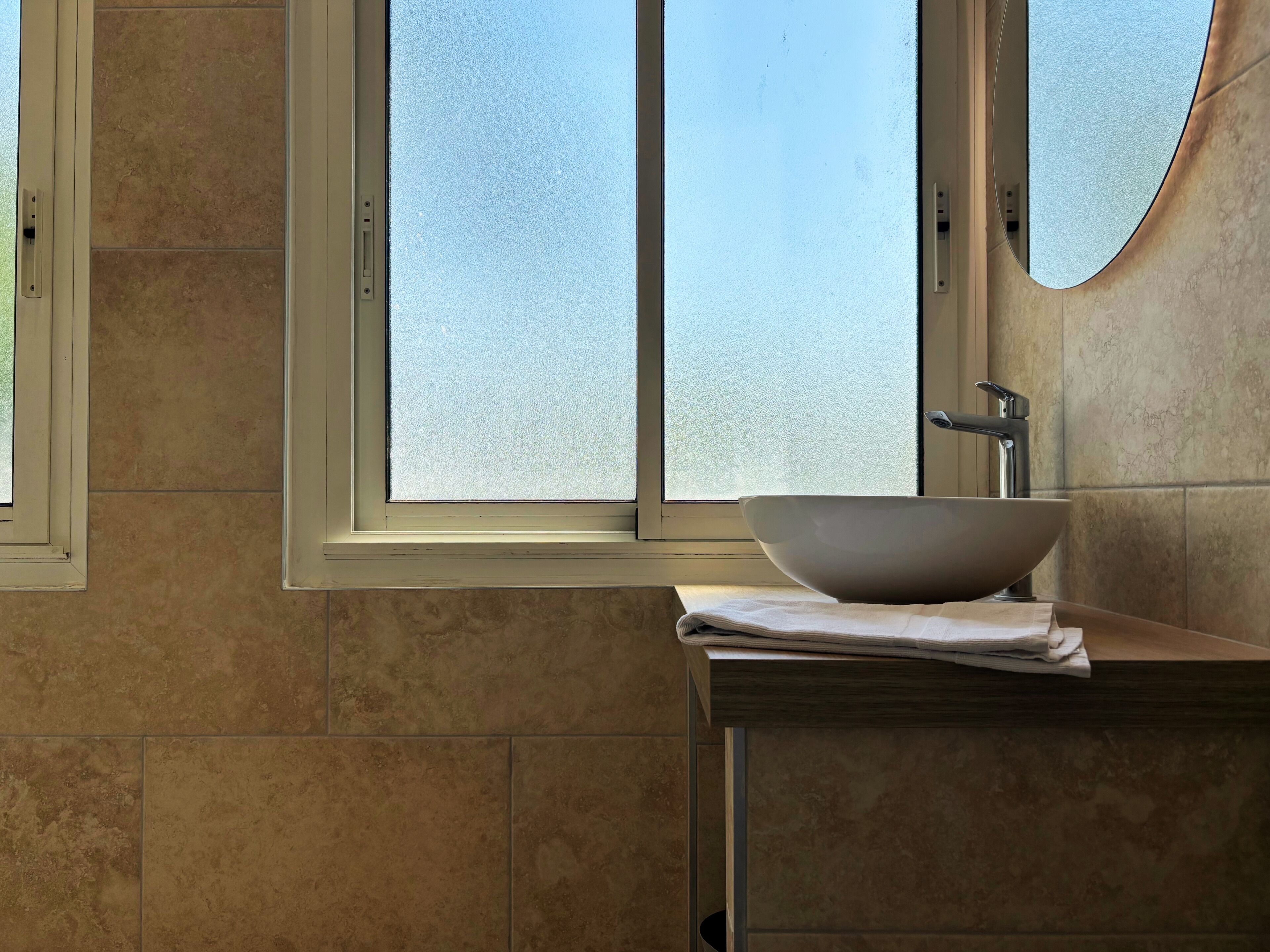 Une salle de bain dotée d’une grande fenêtre, d’un lavabo sur colonne et d’un miroir.