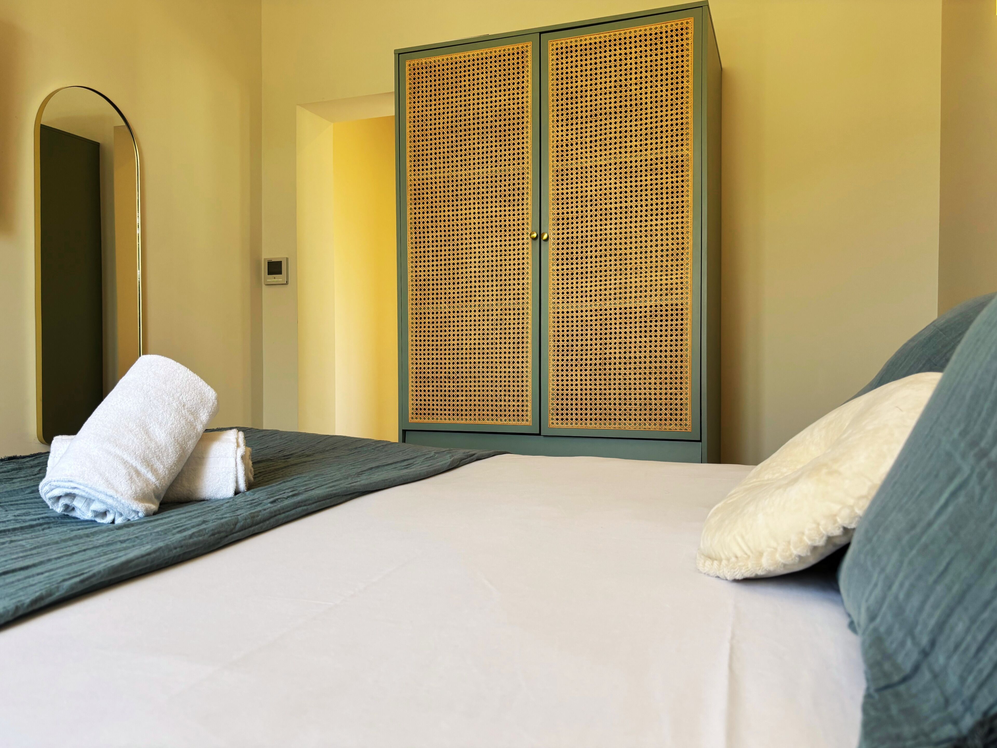 A hotel room with a bed, a large mirror, and a wardrobe with a woven design.