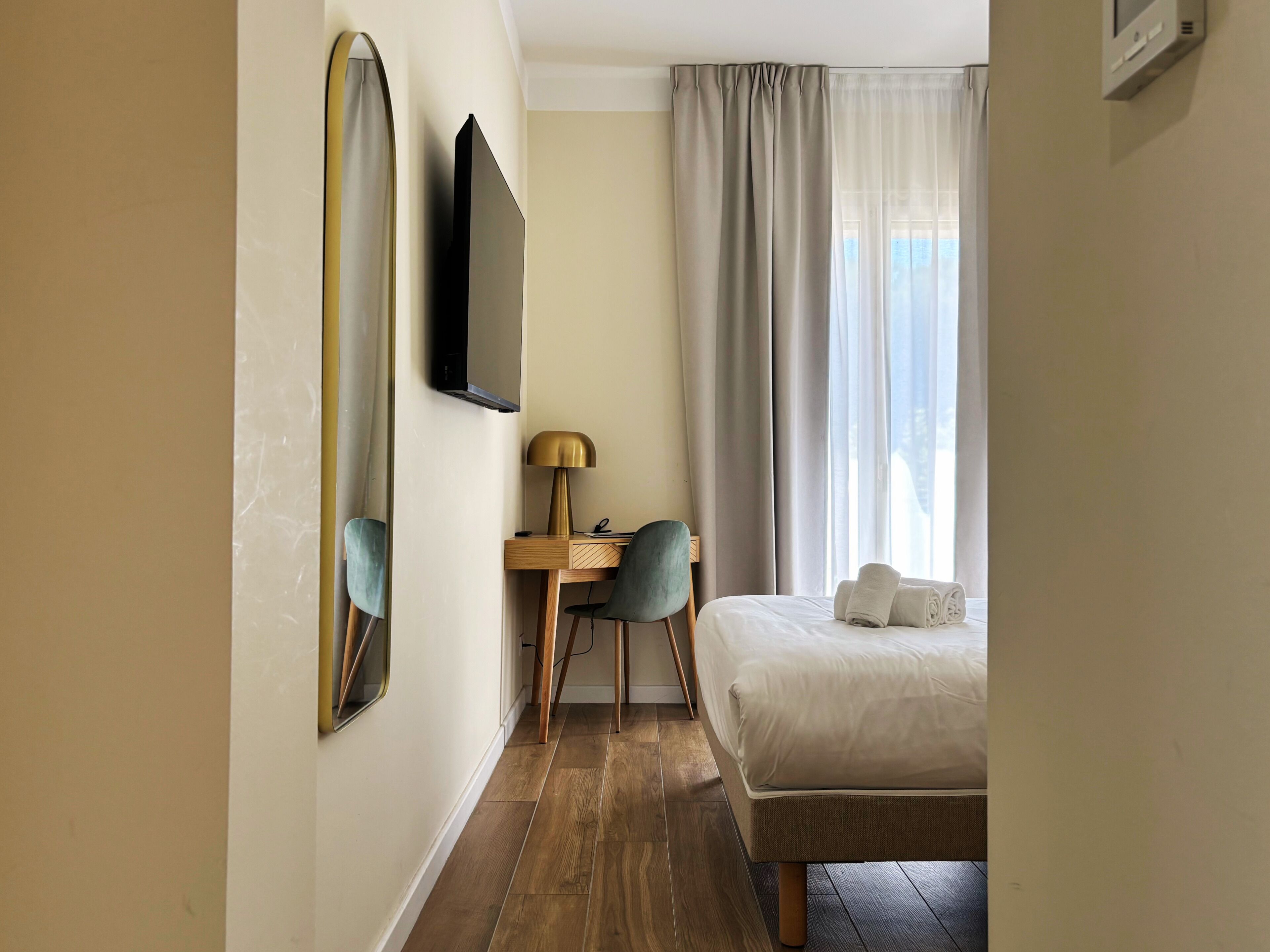 Une chambre d’hôtel avec un lit, un bureau, une chaise, une télévision et une fenêtre avec des rideaux.