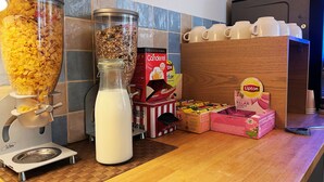 Een ontbijtbuffet met cornflakes, melk en koffiekopjes.