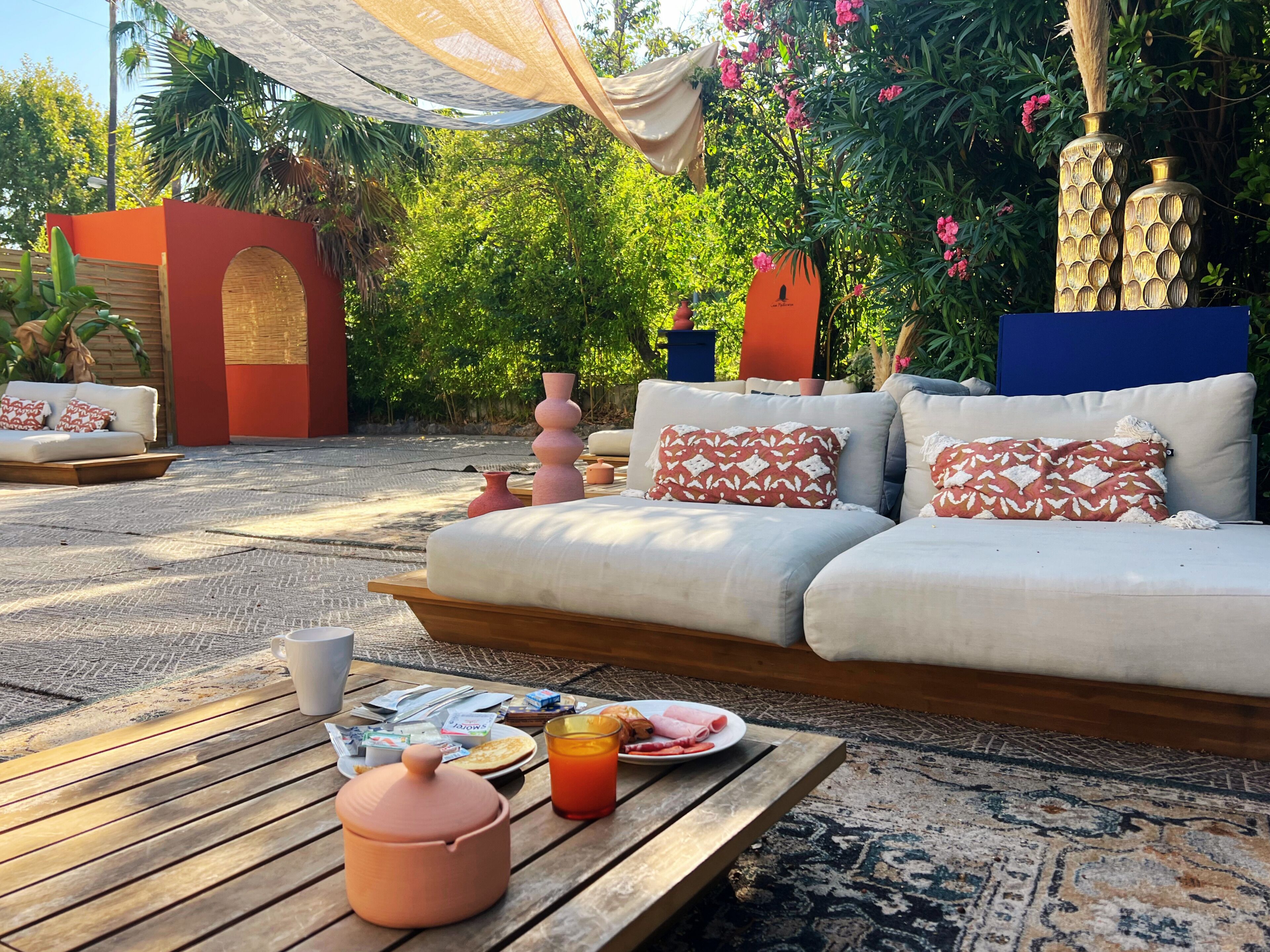 Un espace extérieur aménagé avec un canapé, des coussins, une table garnie de nourriture et de boissons, et des vases décoratifs.