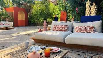 Un espace extérieur aménagé avec un canapé, des coussins, une table garnie de nourriture et de boissons, et des vases décoratifs.