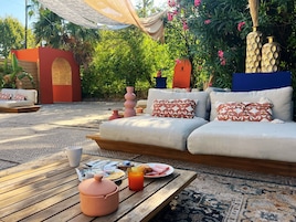 Un espacio al aire libre con sillones, cojines, una mesa con comida y bebidas, y jarrones decorativos.