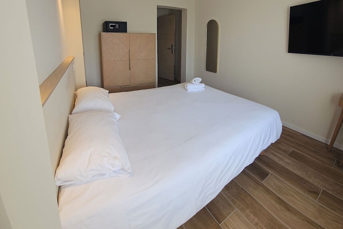 Een hotelkamer met een bed, een aan de muur bevestigde televisie, een handdoek op het bed en een kledingkast.