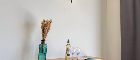 A small wooden table with a vase of dried flowers, a bottle of cologne, and two glasses.