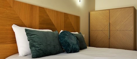 A hotel room with a bed, a wooden headboard, a wall-mounted light, and a wardrobe with a geometric pattern.