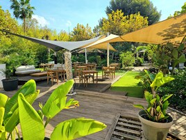 A patio with wooden furniture, a cushioned seating area, and a large umbrella providing shade.