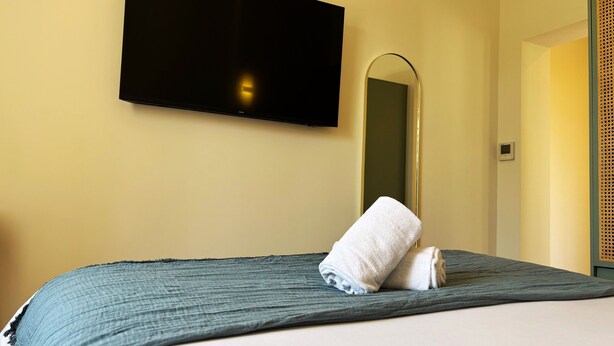 Een hotelkamer met een bed, een flatscreen televisie aan de muur, een spiegel en een deur met decoratief paneel.