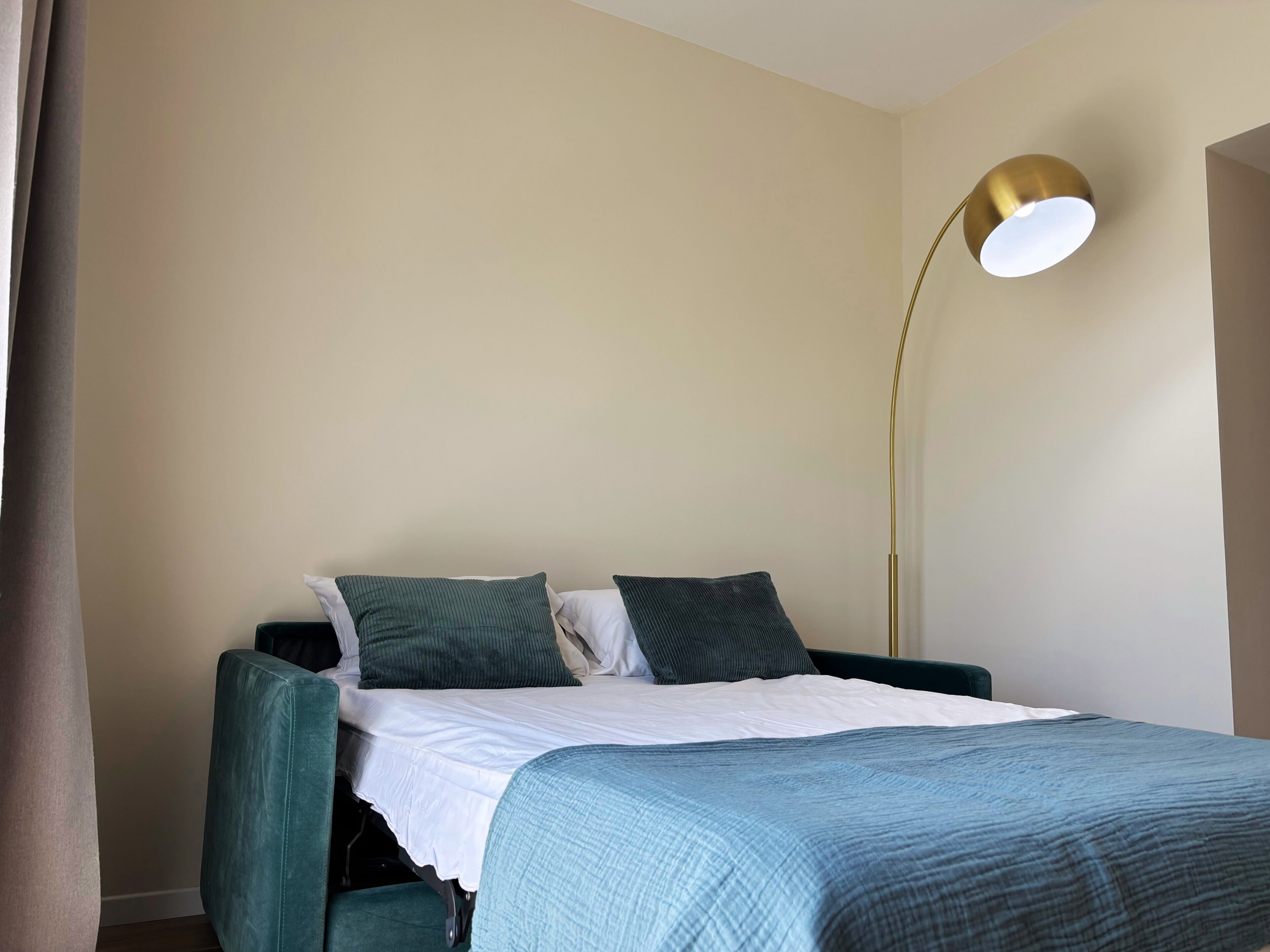 A bed with a white sheet and two pillows, a blue blanket, and a gold floor lamp.