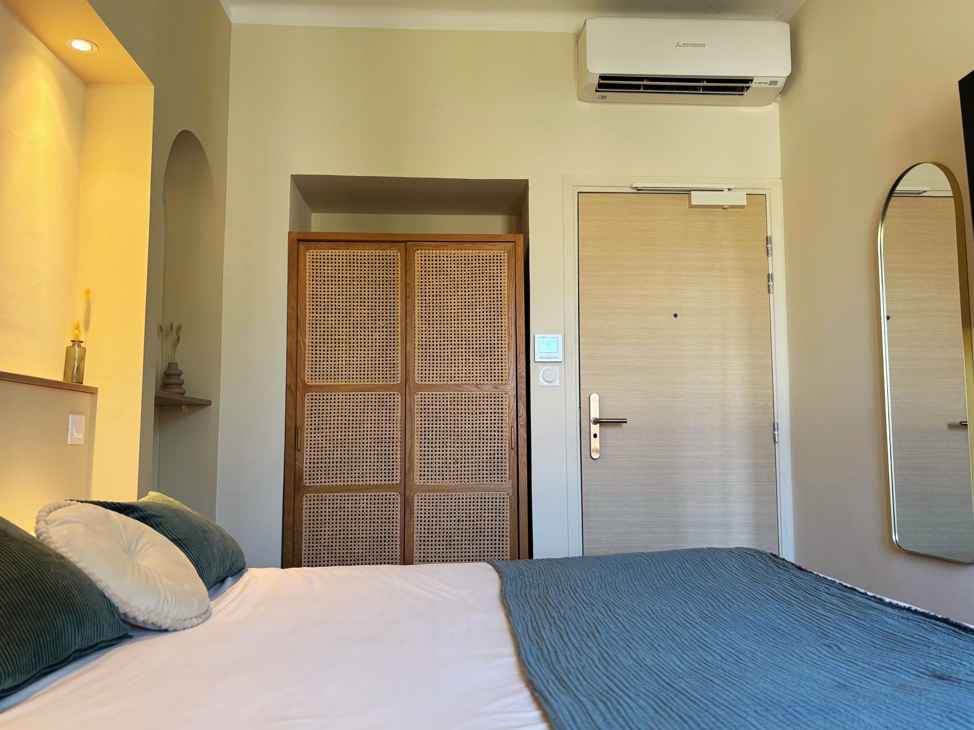 A hotel room with a bed, a wardrobe, a mirror, and an air conditioning unit.