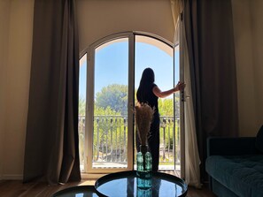 Une pièce dotée d’une grande porte-fenêtre coulissante donnant sur un balcon, d’une table ronde en verre et d’un canapé vert.