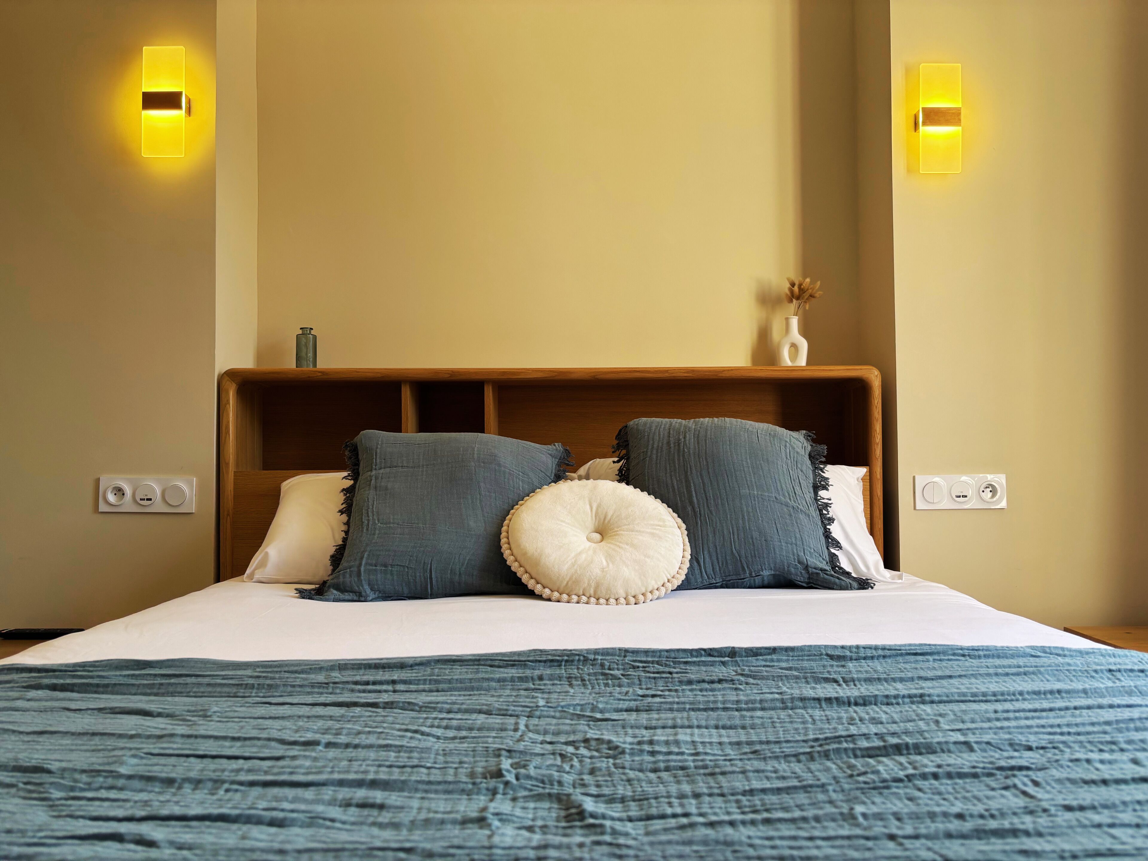 Una habitación de hotel con cama, lámparas de noche y mesita de noche con un florero.