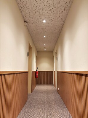 Un couloir doté d’un sol à motifs, de lambris en bois sur les murs, d’un plafond avec des panneaux perforés et d’un extincteur fixé au mur.