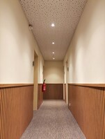 Un pasillo con piso estampado, paneles de madera en las paredes, techo con paneles perforados y un extintor de incendios montado en la pared.