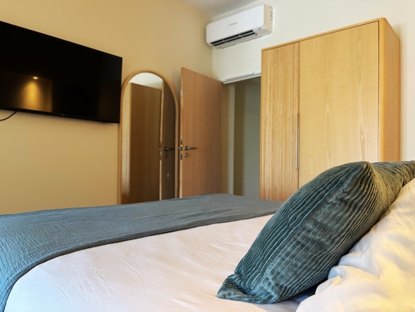A bedroom with a bed, a wardrobe, a mirror, and an air conditioning unit.