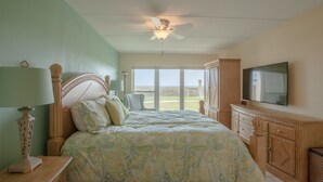 Een slaapkamer met een bed, een plafondventilator, een televisie en uitzicht op de omgeving.