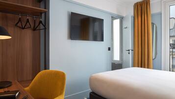 Une chambre d’hôtel comprenant un lit, un bureau avec une chaise, un téléviseur fixé au mur et une porte avec des rideaux.