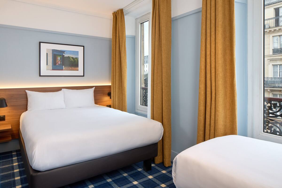 A hotel room with a large bed, a smaller bed, a nightstand, a framed picture on the wall, and a window with curtains.
