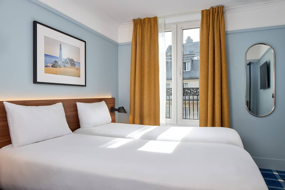 A hotel room with a large bed, a framed picture on the wall, a mirror, and a view of the city through the window.