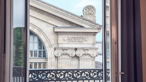 Vista de um edifício com a inscrição 'NORD' em sua fachada, apresentando elementos arquitetônicos clássicos e uma varanda com grades ornamentadas.