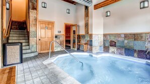 Un área de spa con hidromasaje, escalera de madera, paredes de piedra y techo de madera.