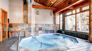 Piscina interior con paredes de piedra y vigas de madera, un banco y vistas al exterior.