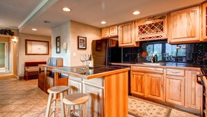 Una cocina con armarios de madera, una isla central con taburetes, un refrigerador y un lavamanos.