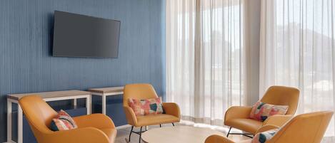 A modern living room with a round coffee table, two orange armchairs, a small white side table, and a flat-screen TV mounted on a blue wall.