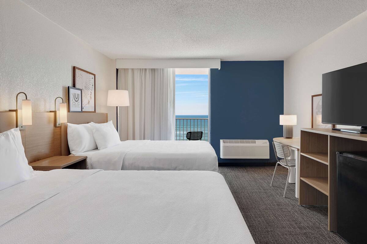 Habitación de hotel con dos camas, un escritorio, un televisor y vista al mar.