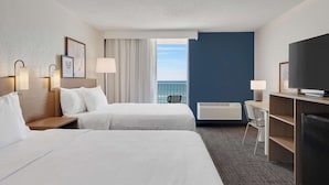 Habitación de hotel con dos camas, un escritorio, un televisor y vista al mar.